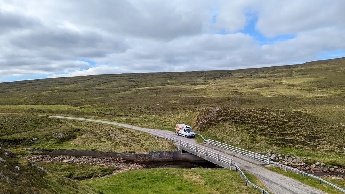 Pechhulp en vervangend vervoer voor je bedrijfswagen Witte bestelbus onderweg over een brug in een groen landschap