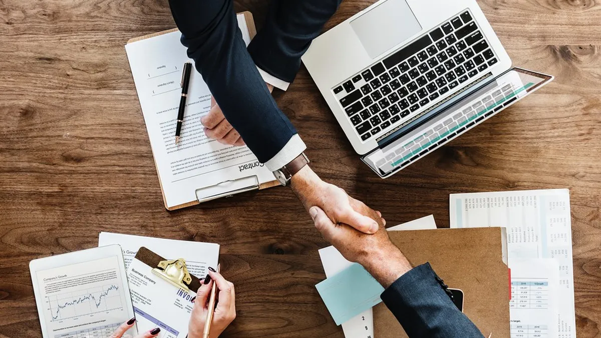 Rechtsbijstand bij je bedrijfswagenverzekering: nodig of niet? Twee mensen schudden handen boven een bureau met contracten en laptop
